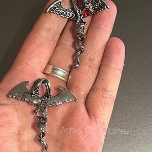 May include: Two silver dragon pendant necklaces with red gemstone accents. The dragons are curled in a spiral shape.