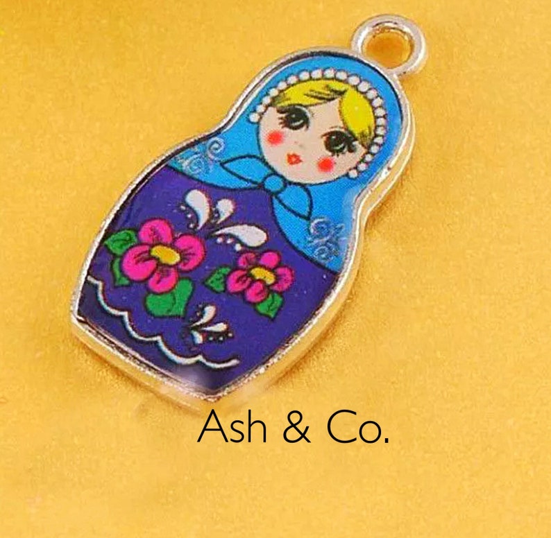 May include: A silver charm in the shape of a Russian nesting doll. The doll is painted with blue, purple, pink, yellow, and green colors. The doll has a smiling face and a floral pattern.