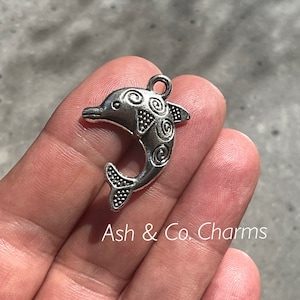 May include: Silver-toned dolphin charm featuring intricate swirl designs. The charm has a loop at the top for attaching to jewellery or other crafts.