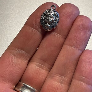 May include: Silver lion head charm pendant. The lion's mane is detailed and the face is fierce.