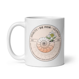 Puede incluir: Taza de cerámica blanca con un diseño circular que presenta una concha, una flor y el texto "SPIRITS DE FEM SÉANCES EST. 1896 ANNA CASSEL CORNELIA CEDARBURG HILMA AF KLINT SIGRID HEDMAN MATHILDA NILSSON".