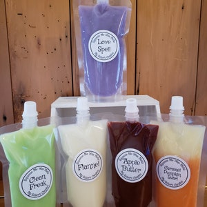 May include: Five pouches of wax melts in various colors and scents. The scents are Love Spell, Clean Freak, Flannel, Apple Butter, and Caramel Pumpkin Swirl. Each pouch has a white label with the scent name and "Squeeze Me Wax Melts" and "My Sister's Candles".