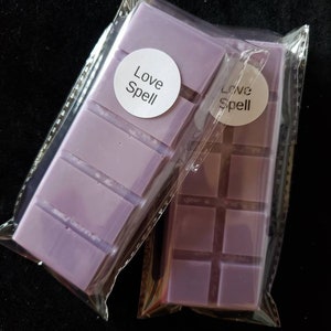 May include: Two purple wax melts in clear plastic packaging. Each melt has a white circle label with the text "Love Spell" printed in black.