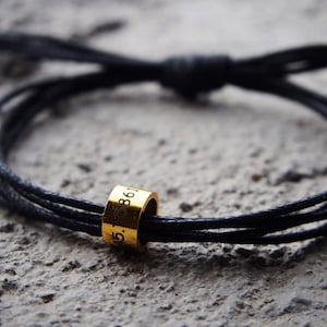 Peut inclure: Un bracelet en cordon noir avec un cordon doré gravé du numéro "45.75861".
