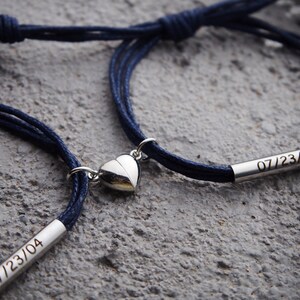 May include: Two matching blue cord bracelets with a silver heart charm and a silver bar engraved with the date "07/23/04".