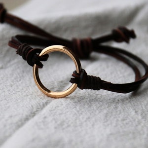 May include: A brown leather bracelet with a gold circle charm.