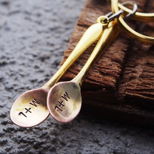 May include: Two gold-toned spoons with a ring attached. The spoons are engraved with the letters "L+W".
