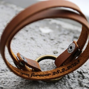 Op de afbeelding: Een bruin leren armband met een zilveren ring en de inscriptie "you forever 28.2.2023".