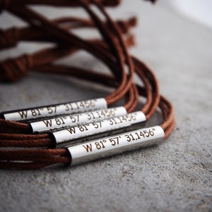Op de afbeelding: Vier bruine leren armbanden met zilveren metalen bedels gegraveerd met de coördinaten "W 81° 57' 31.1456"