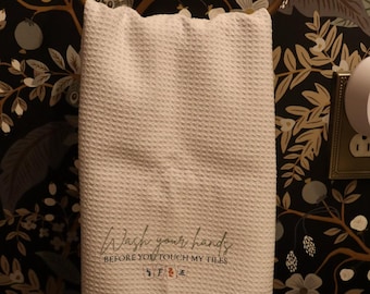 May include: A white waffle-weave hand towel hanging on a brass ring. The towel features the printed text "Wash your hands BEFORE YOU TOUCH MY TILES" in a mix of script and block lettering, followed by four small colorful mahjong tile icons.