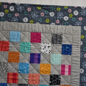 May include: A patchwork quilt with a gray background and colorful squares. The quilt is edged with a gray fabric with a white daisy print.