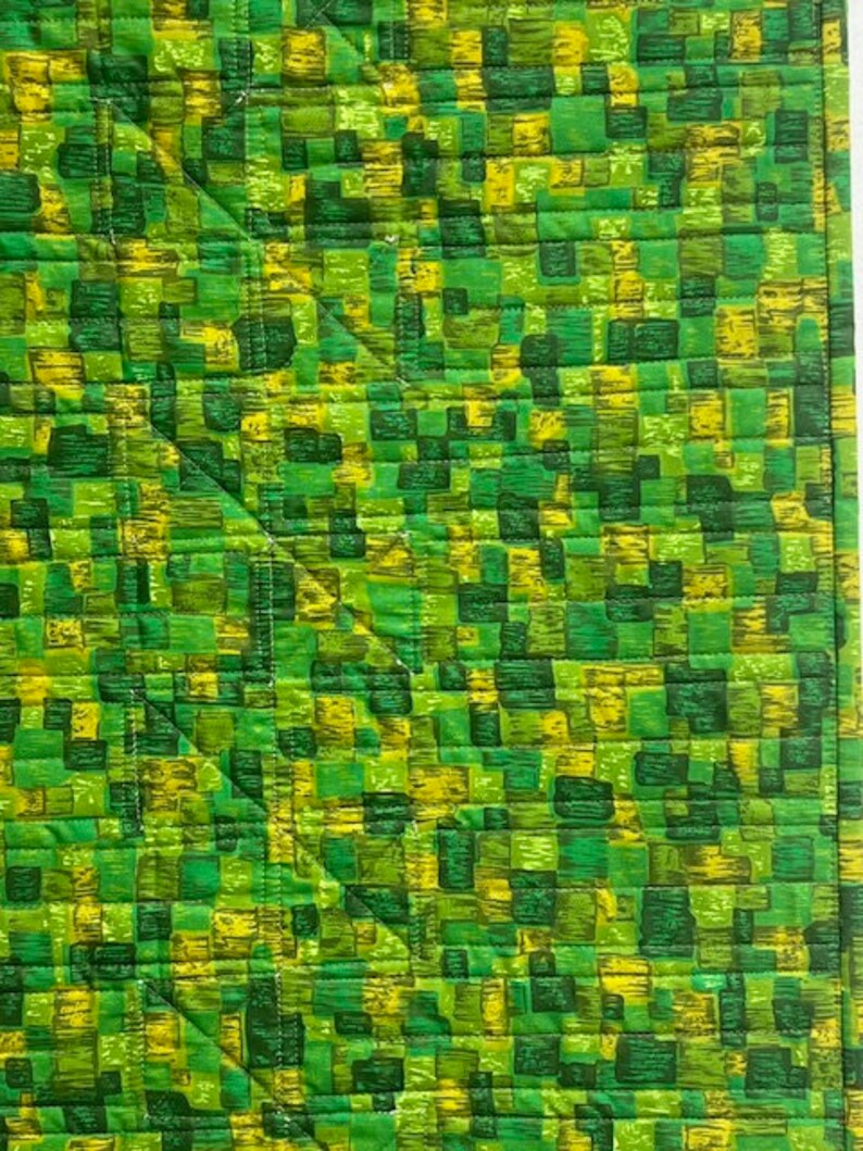 K&ouml;nnte beinhalten: Gr&uuml;ner und gelber gesteppter Stoff mit einem geometrischen Muster aus Quadraten und Rechtecken.