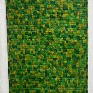 K&ouml;nnte beinhalten: Eine gr&uuml;ne und gelbe Steppdecke mit geometrischem Muster. Die Steppdecke besteht aus Quadraten und Rechtecken, und das Muster wiederholt sich &uuml;ber die gesamte Steppdecke.