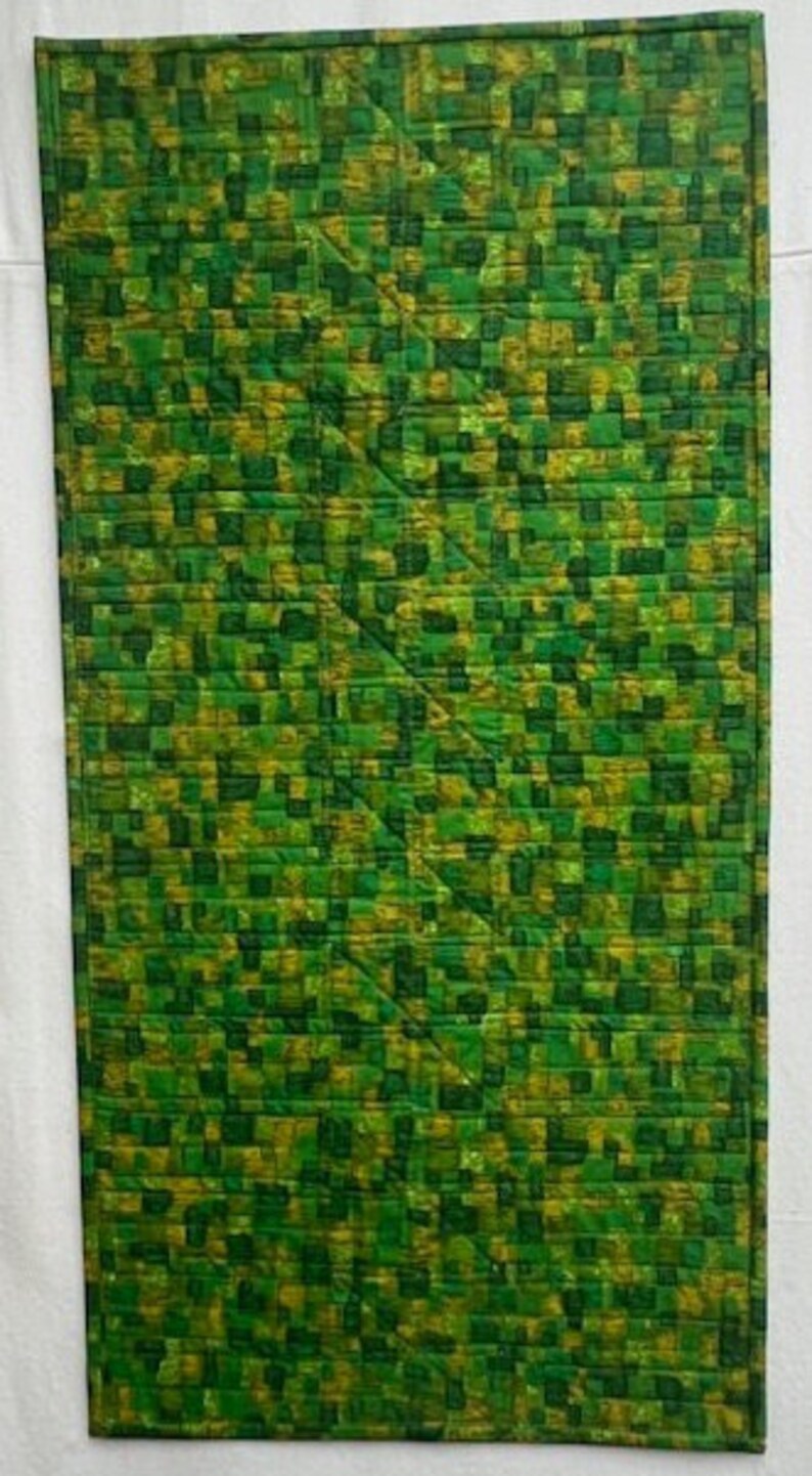 K&ouml;nnte beinhalten: Eine gr&uuml;ne und gelbe Steppdecke mit geometrischem Muster. Die Steppdecke besteht aus Quadraten und Rechtecken, und das Muster wiederholt sich &uuml;ber die gesamte Steppdecke.