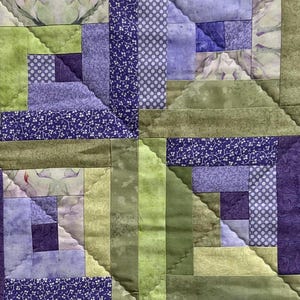 May include: A quilt with a log cabin pattern in shades of green and purple. The quilt is made of different fabrics with floral and geometric designs.
