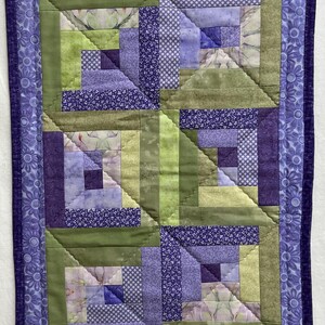 May include: A purple and green quilt with a log cabin pattern. The quilt is made of various fabrics with floral and geometric designs.