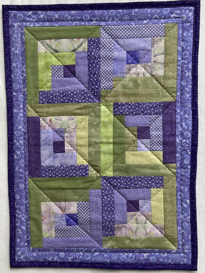 May include: A purple and green quilt with a log cabin pattern. The quilt is made of various fabrics with floral and geometric designs.