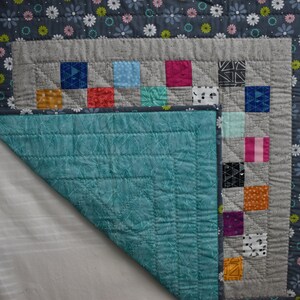 May include: A teal blue quilted fabric with a gray and white patterned fabric border. The gray fabric has a patchwork design with squares of various colors and patterns.