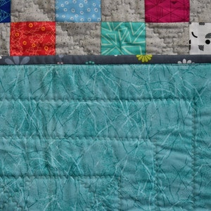 May include: A teal blue quilted fabric with a white pattern of thin lines and branches. The fabric has a gray border with white flowers.