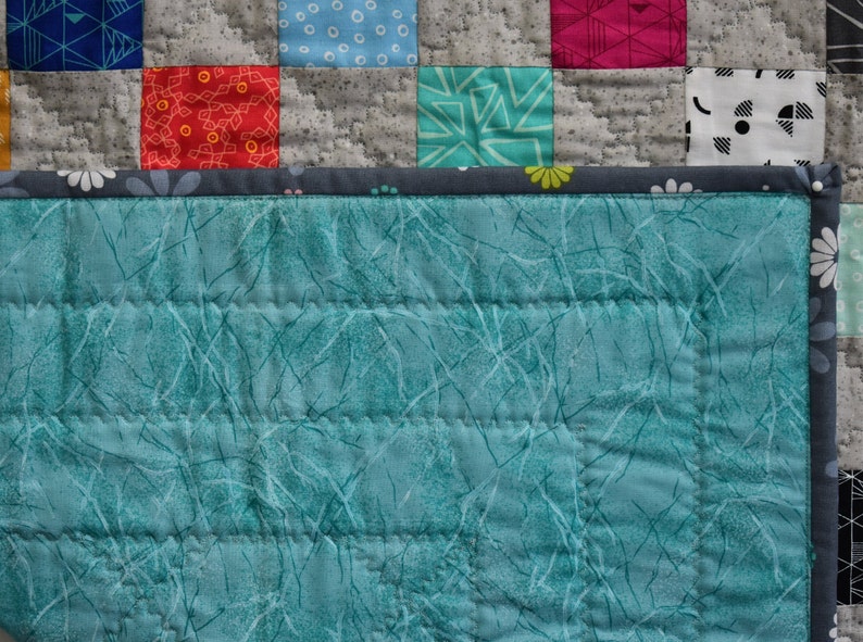 May include: A teal blue quilted fabric with a white pattern of thin lines and branches. The fabric has a gray border with white flowers.