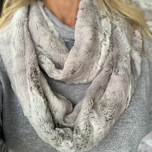Könnte beinhalten: Ein weicher, grauer Kunstfell-Infinity-Schal. Der Schal ist aus einem plüschigen, flauschigen Material gefertigt und perfekt, um sich im Winter warm zu halten.