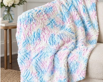 May include: A plush throw blanket featuring a textured, ruffled surface with a tie-dye pattern in shades of white, light blue, and soft pink. The fabric has a high-pile, curly appearance that creates a dimensional look across the entire piece.