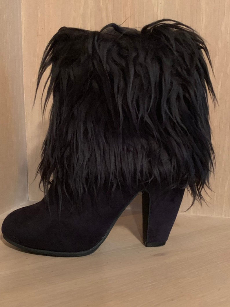 May include: Black ankle boot with a faux fur upper. The boot features a rounded toe and a block heel. The faux fur is long and shaggy, adding a unique texture to the design. The heel is approximately 3 inches (7.6 cm) high.