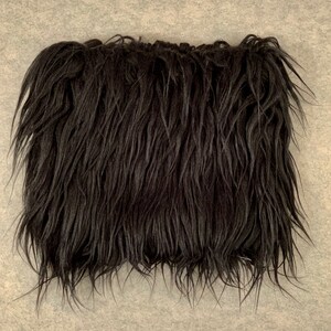 May include: A rectangular piece of black faux fur with long, shaggy strands. The fur has a dense, textured appearance, with individual fibers extending outwards. The overall color is a deep, solid black, creating a dramatic effect.