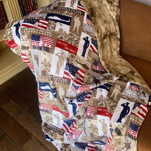 May include: A patriotic throw blanket featuring a patchwork design of American flags, camouflage patterns, and silhouettes of soldiers. The text "Freedom is not free" and "Thank you" are repeated throughout the design. The blanket is made of a soft, plush fabric.