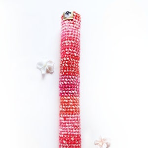 May include: A long, rolled up crocheted rug in shades of pink and red. The rug is made with a textured, chunky yarn.