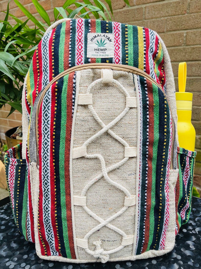 May include: A multi-coloured striped hemp backpack with a white hemp rope design. The backpack has a small pocket on the front and a label that reads "Himalayan Hemp THC Free Made in Nepal".