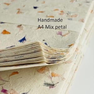 May include: A stack of handmade A4 paper sheets with mixed flower petals embedded in the paper. The paper is cream colored with orange, purple, and blue flower petals.