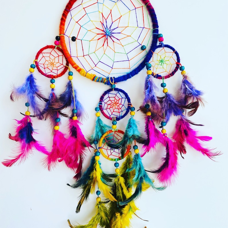 May include: A colorful dreamcatcher with a rainbow-colored outer ring and smaller inner rings. It features a variety of feathers in shades of purple, pink, teal, and yellow.