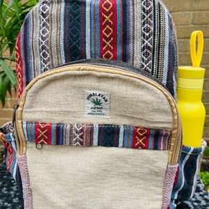 May include: A beige hemp backpack with colourful striped fabric accents. The backpack has a zipped pocket on the front and a label that reads "Himalayan Hemp THC Free Made in Nepal".