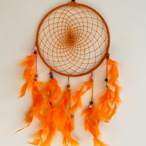 May include: Orange dream catcher with a circular woven net and orange feathers hanging from the bottom. The net is decorated with colorful beads.