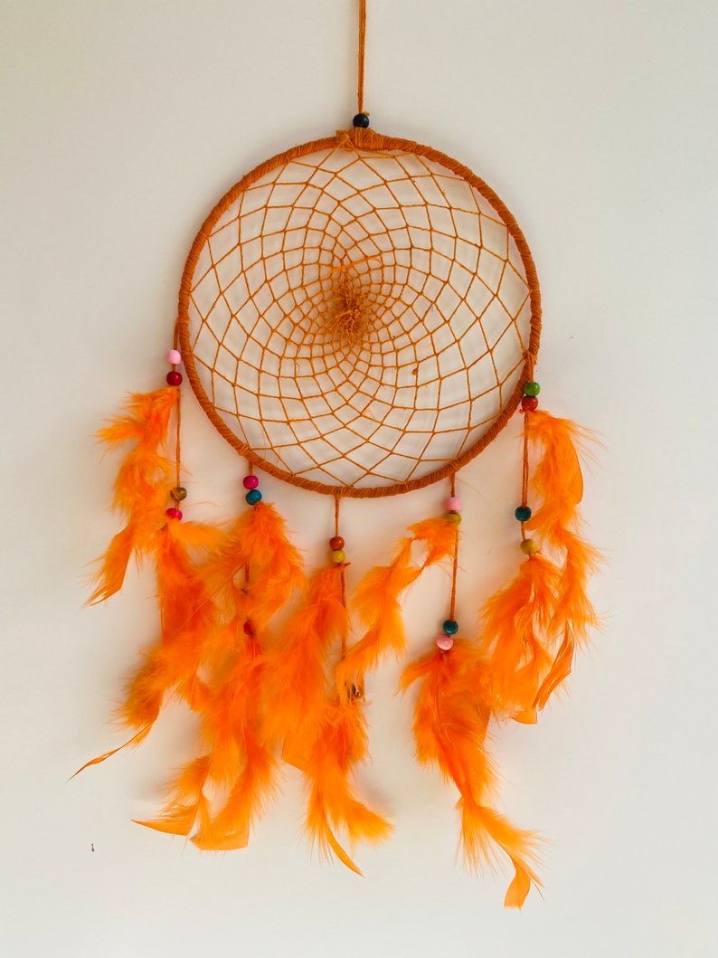 May include: Orange dream catcher with a circular woven net and orange feathers hanging from the bottom. The net is decorated with colorful beads.