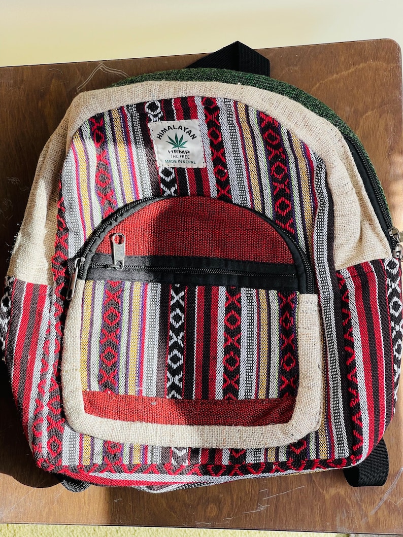 May include: A red, black, and white striped hemp backpack with a brown leather strap and a label that reads "Himalayan Hemp The Free Made in Nepal".