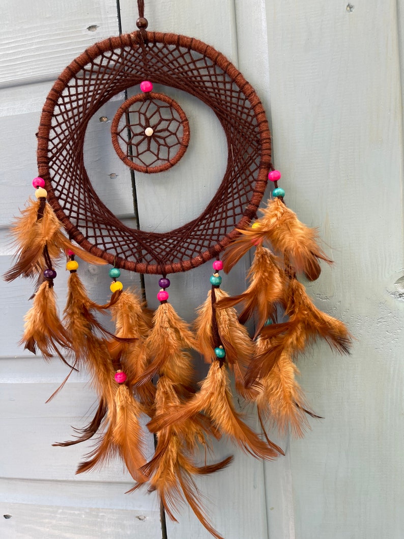 May include: A brown dreamcatcher with a smaller brown dreamcatcher inside. The larger dreamcatcher has brown feathers and colorful beads.