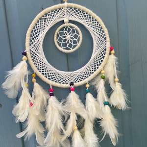 May include: White dream catcher with white feathers and colorful beads. The dream catcher has a smaller circle in the center.