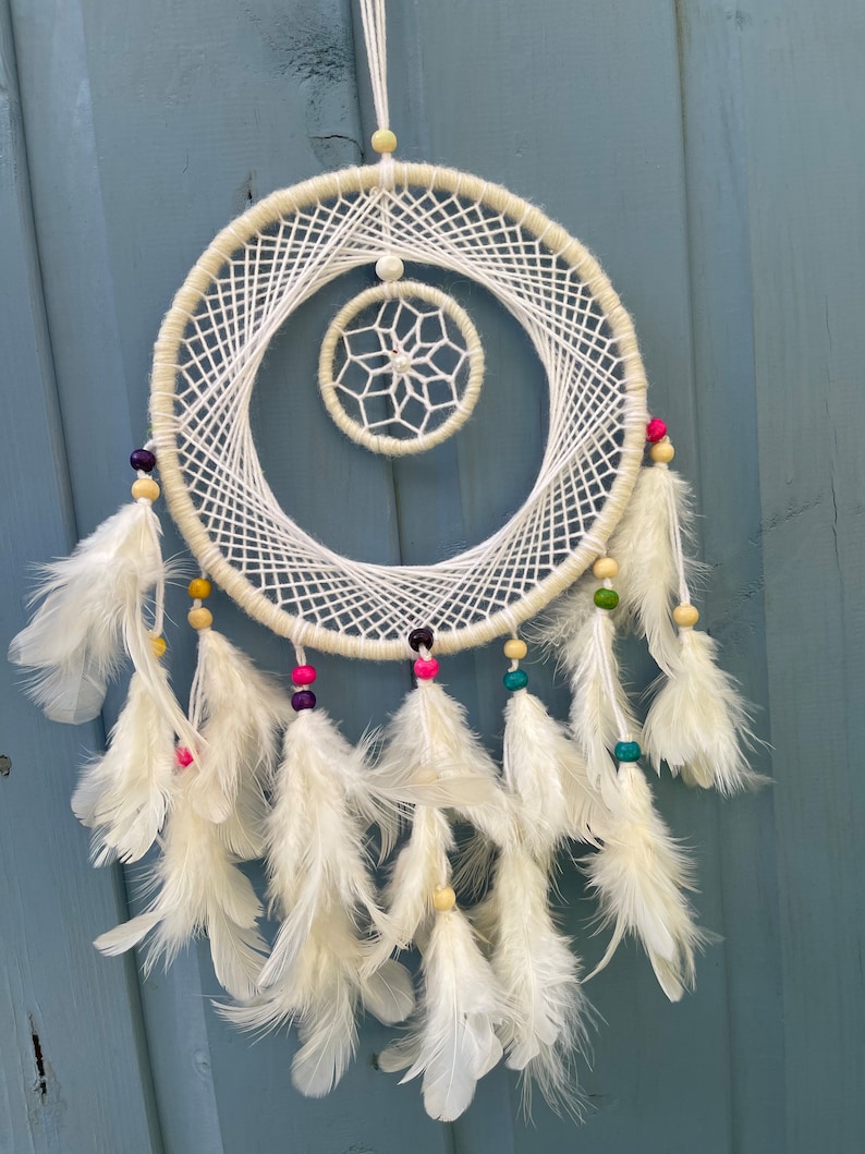 May include: White dream catcher with white feathers and colorful beads. The dream catcher has a smaller circle in the center.