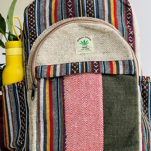 May include: A multi-coloured striped hemp backpack with a large front pocket. The pocket has a brown zipper and a small patch with the text "Himalayan Hemp THC Free Made in Nepal".