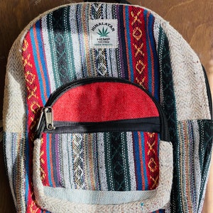 May include: A multi-colored striped hemp backpack with a red zippered pocket and a label that reads "Himalayan Hemp THC Free Made in Nepal".