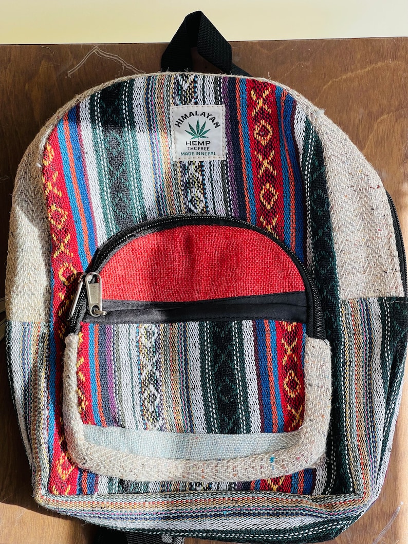 May include: A multi-colored striped hemp backpack with a red zippered pocket and a label that reads "Himalayan Hemp THC Free Made in Nepal".