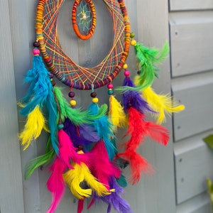 May include: A colorful dreamcatcher with a rainbow of feathers and beads. The dreamcatcher has a circular frame with a smaller circle in the center. The feathers are arranged in a cascade around the dreamcatcher.