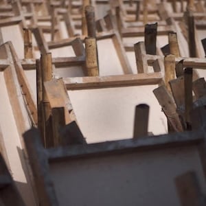 May include: A close-up of a stack of wooden frames, likely used for making paper or other crafts. The frames are made of light-colored wood and have a rough, unfinished texture.