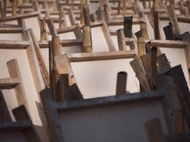 May include: A close-up of a stack of wooden frames, likely used for making paper or other crafts. The frames are made of light-colored wood and have a rough, unfinished texture.