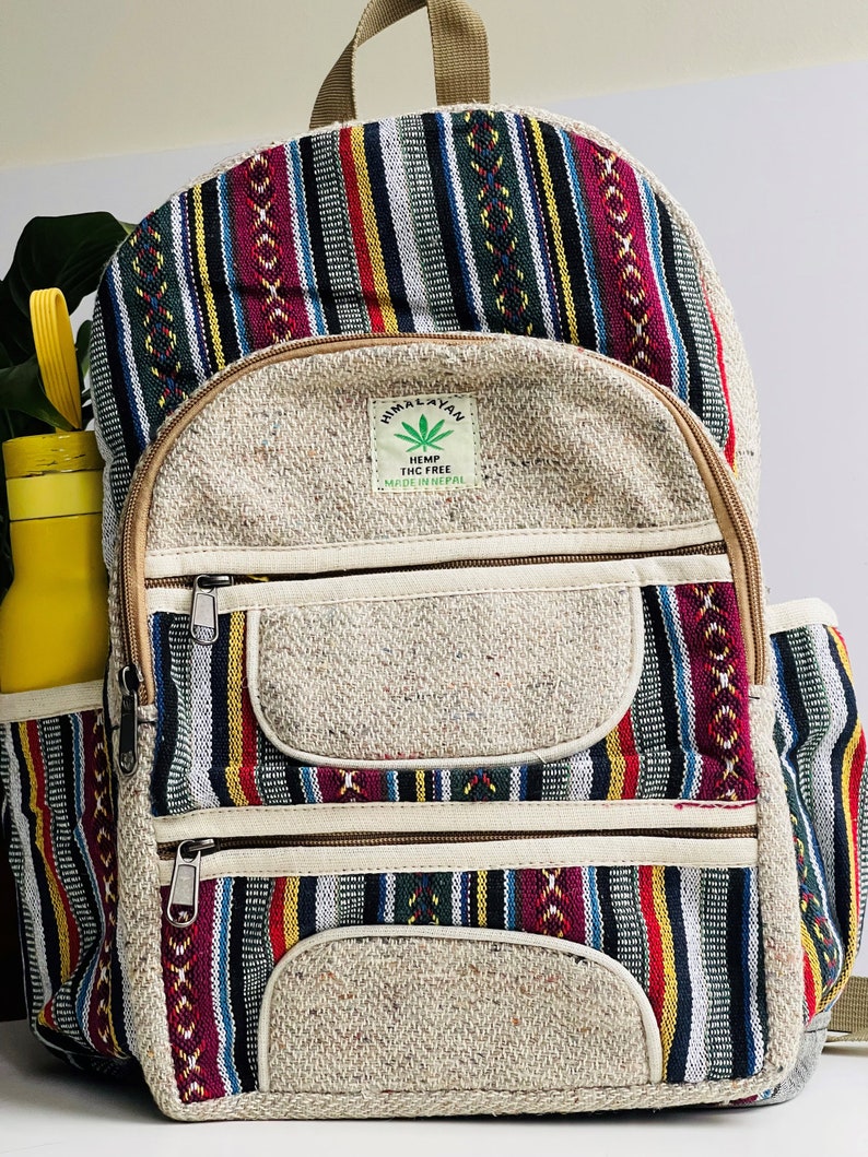 May include: A striped hemp backpack with a front pocket and two zippered compartments. The backpack has a brown leather strap and a label that reads "Himalayan Hemp THC Free Made in Nepal".