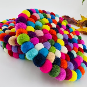 May include: A colorful round felt coaster made of many small balls of felt in various colors, including red, blue, green, yellow, pink, and purple.