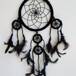 May include: Black dreamcatcher with feathers. The dreamcatcher has a large circular hoop with a web-like design and three smaller hoops with similar designs. The dreamcatcher is adorned with black feathers.