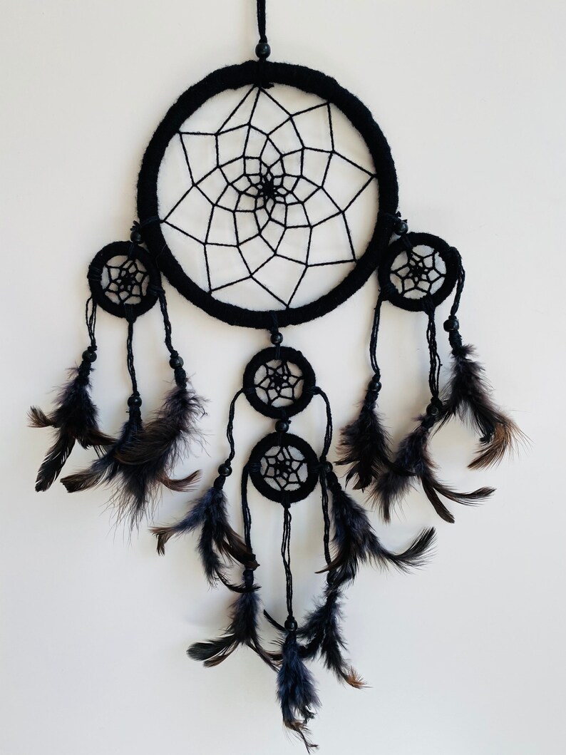 May include: Black dreamcatcher with feathers. The dreamcatcher has a large circular hoop with a web-like design and three smaller hoops with similar designs. The dreamcatcher is adorned with black feathers.
